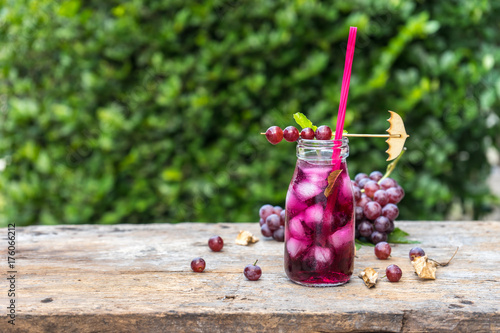 cool grape juice in glass jar on old wood with tree background. dried leaf autumn concept.