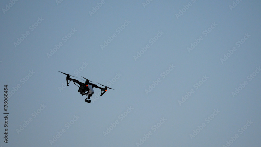Fototapeta premium Black drone quadcopter with camera flying over blue sky. Black drone in the sky. Flying quadrocopter drone in the sky with mounted digital camera for video and photo productions
