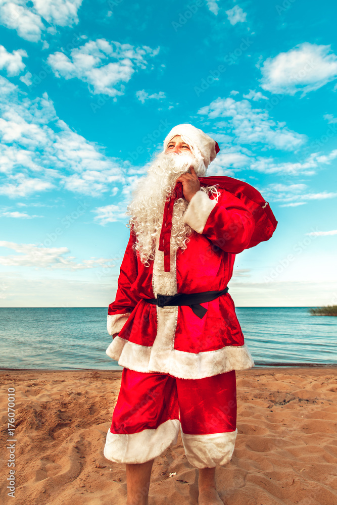 Obraz premium Santa Claus with a bag of gifts on the beach. The symbol of Christmas.
