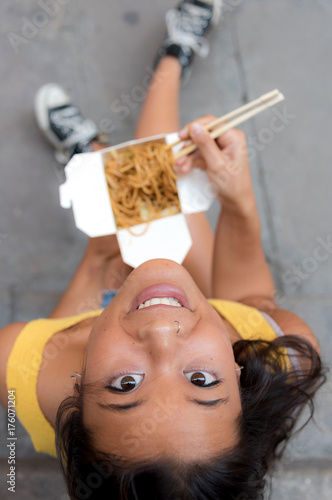 Young asiatic woman eating a chinese take-away on her doorstep