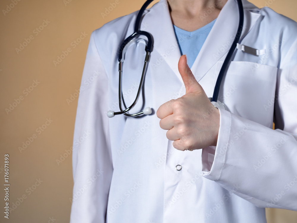 Female doctor showing thumb up. Female doctor with a stethoscope gesticulating on a beige background. Female doctor showing thumb up. Female doctor with a stethoscope gesticulating on a beige background.