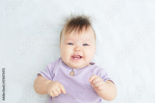 Happy smiling Infant baby portrait looking at camera lying on white blanket