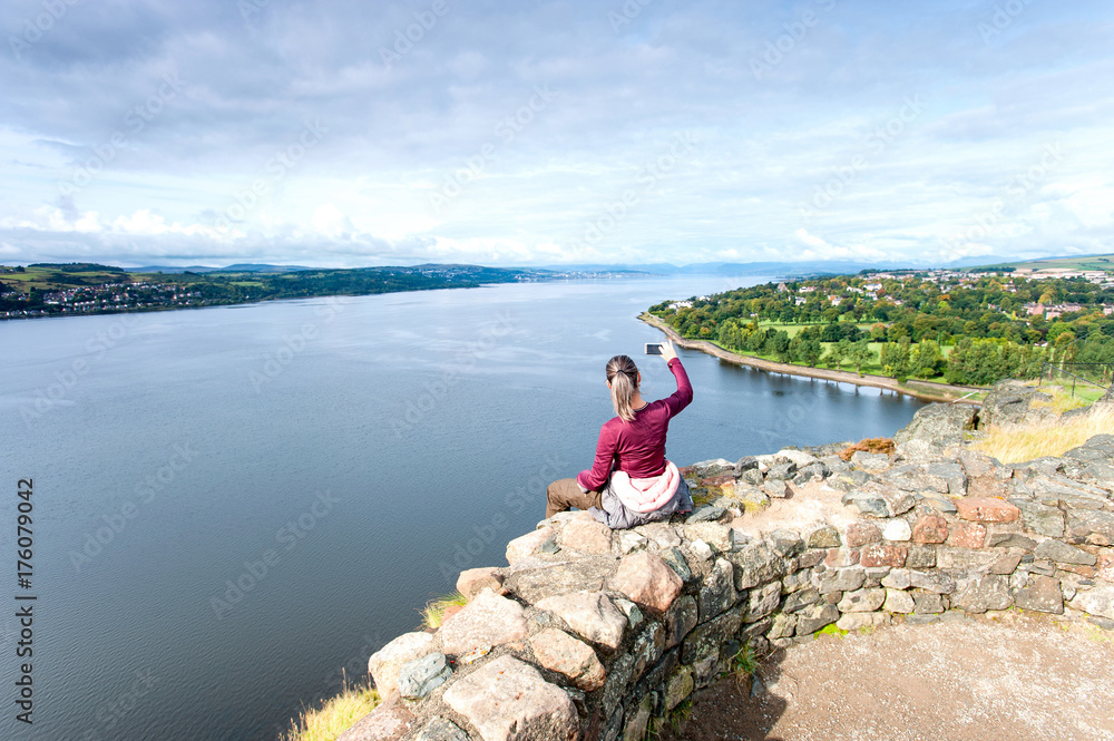 Woman traveller sitting on mountain top making picture by smartphone