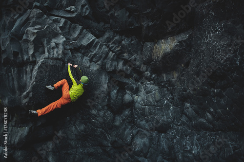 male rock climber. rock climber climbs on a black rocky wall on the ocean bank in Iceland, Kirkjufjara beach. man makes hard move without rope. photo