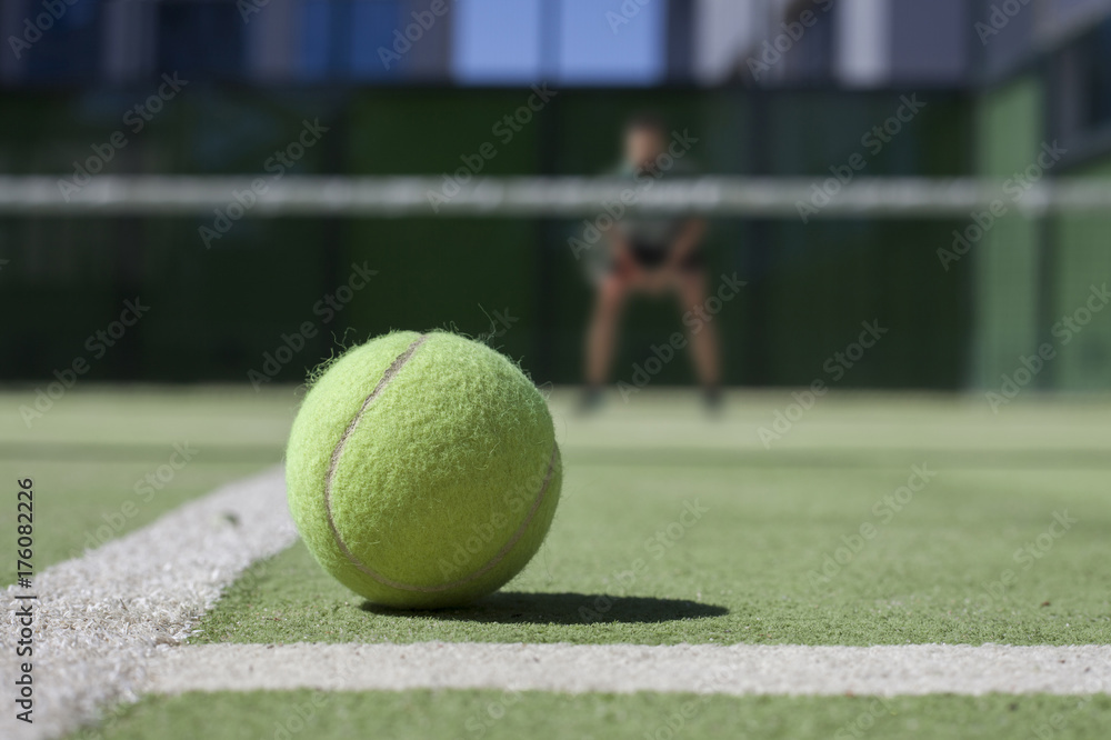 Tennis ball on a tennis court with tennisplayer out of focus.