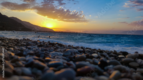 summer evening at the beach during the sunset with stones sand waves and people swimming © Constantine_papp