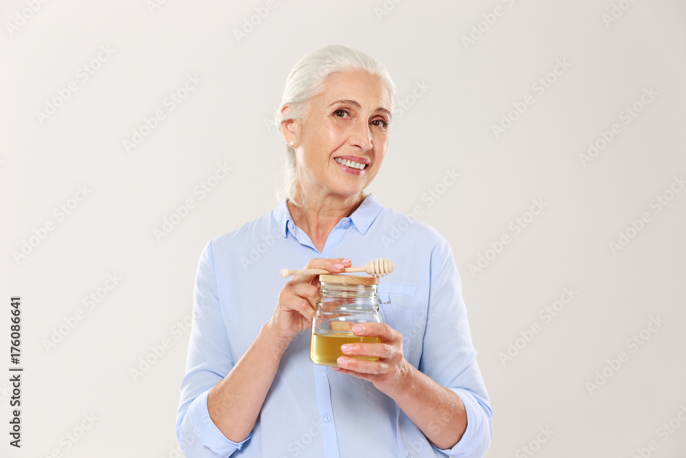 Close-up portrait of charming mature woman, holding honey jar with spoon, looking at camera Close-up portrait of charming mature woman, holding honey jar with spoon, looking at camera