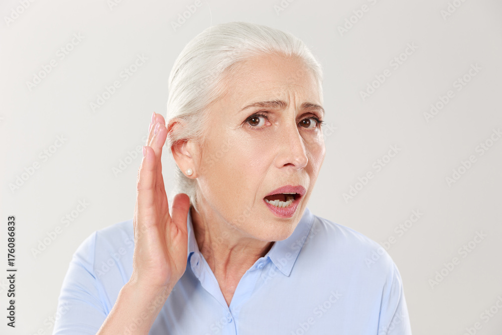 Close-up of charming elderly woman, holding hand by her ear and struggling to hear something Close-up of charming elderly woman, holding hand by her ear and struggling to hear something