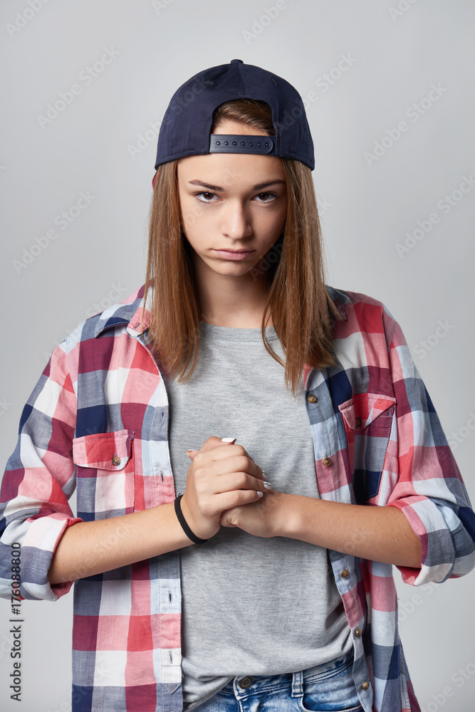 Angry teen girl wearing checkered shirt and baseball cap over grey  background looking at camera sullen and clenching her fists , front view  Stock Photo | Adobe Stock