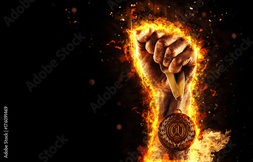 Man's hand in a fire is holding up gold medal. Winner in a competition.
