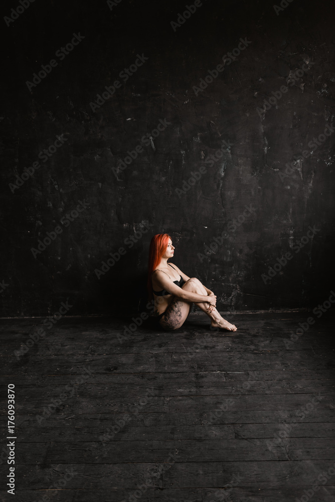 Long legs girl, woman sit on floor in black lingerie in tattoo on black background