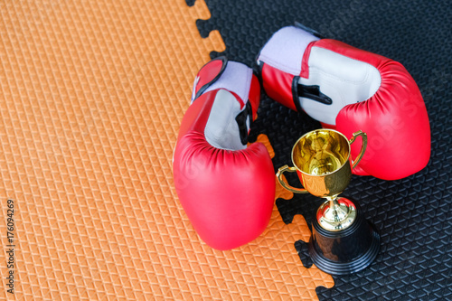 Golden trophy cup with red boxing gloves on black and orange background photo