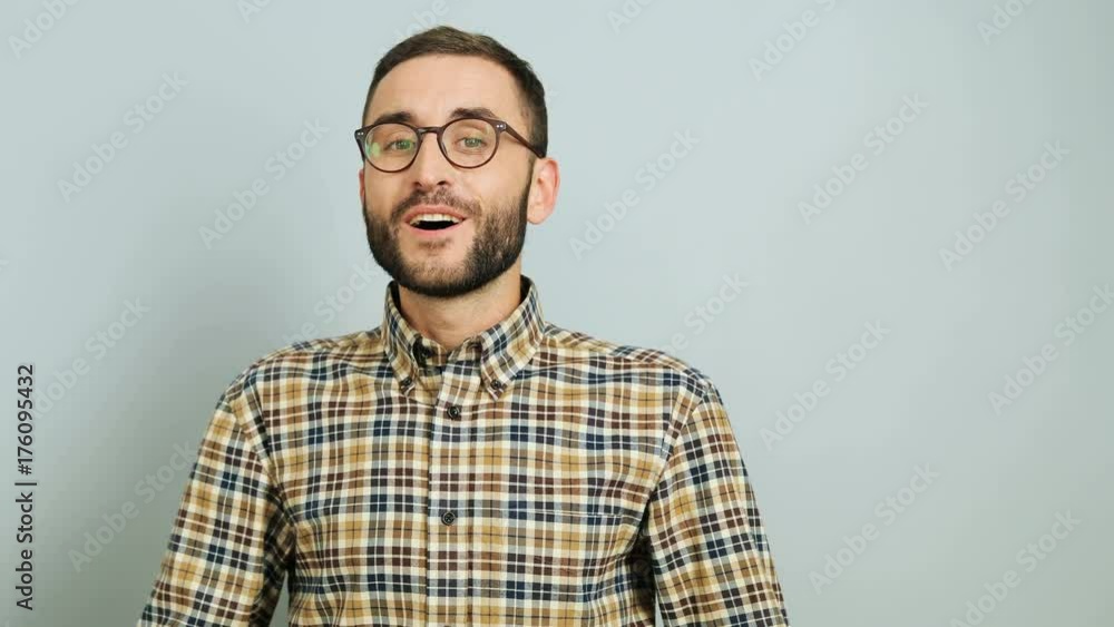 Close up shot of a young caucasian man in a casual shirt showing emotion of amasement and happiness on the grey background. Outdoor shot. Close up shot of a young caucasian man in a casual shirt showing emotion of amasement and happiness on the grey background. Outdoor shot.