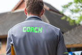 back of a male coach's grey shirt with the green word Coach written on it