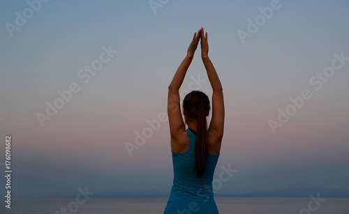  woman practicing yoga on the beach at sunset, back view