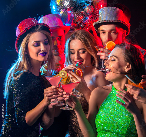 Cocktail party with group people dancing and drink cocktail. Happy women in evening dresses and men have fun in night club and disco ball background. Rest after a hard day at work.