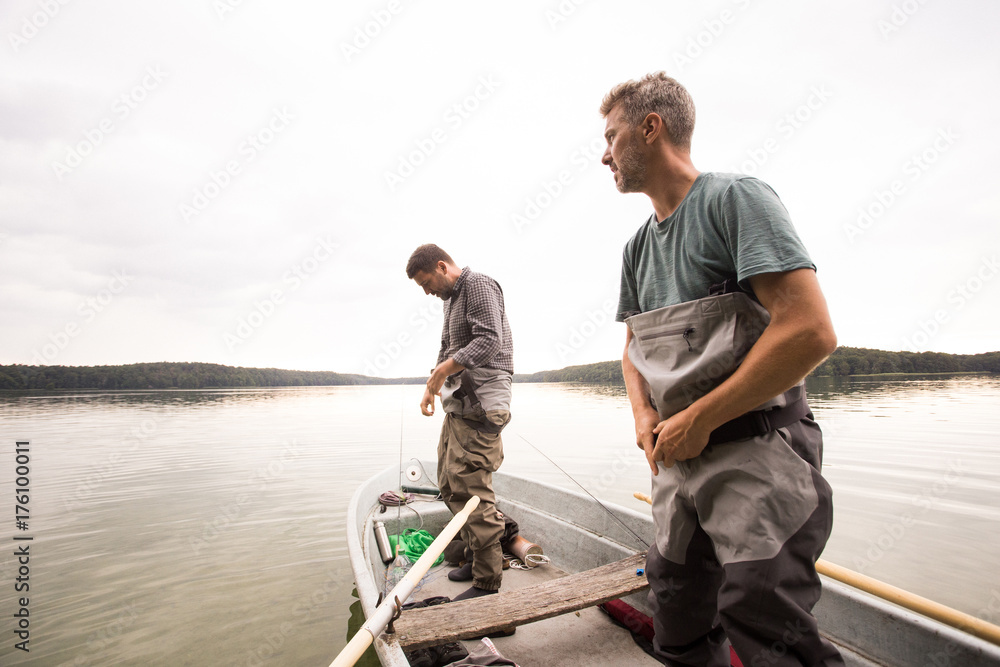 Two mature men are putting on waders before fly fishing from a lake. Two mature men are putting on waders before fly fishing from a lake.