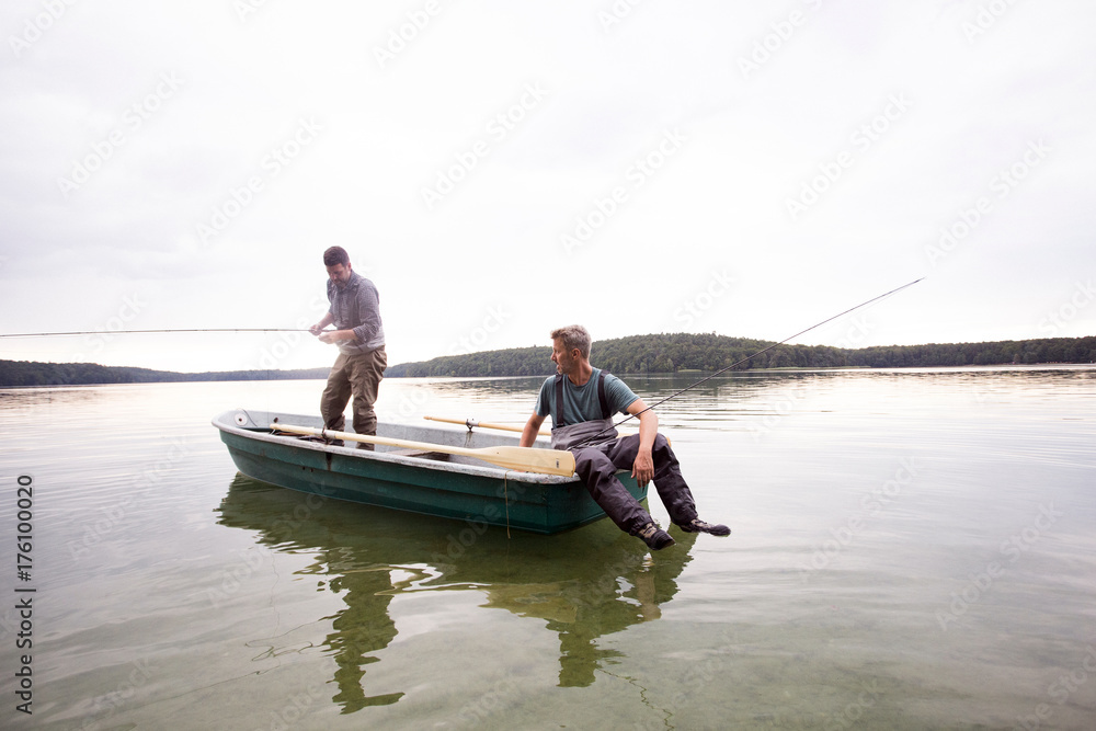 Two men in waders are fly fishing from a boat in a lake. Stock