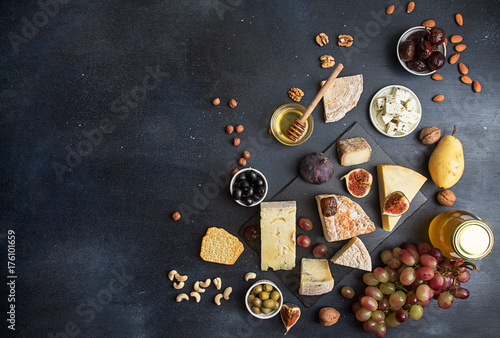 Food background with cheese. Blocks of moldy cheese, grapes, figs, honey, pear, dates, pickled prunes, nuts over on dark background. Copy space. Top view