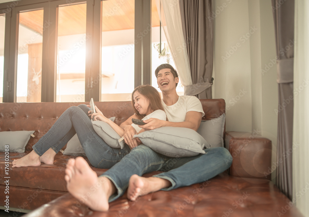 Asian couple watching TV sitting on a couch at home cheerful