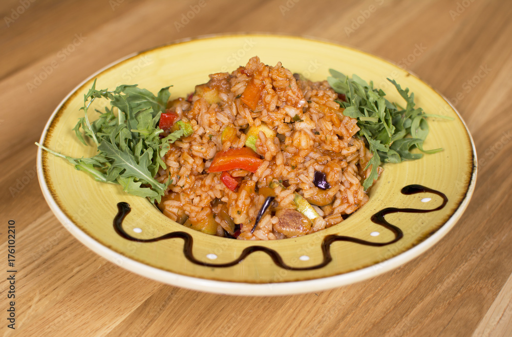 A plate of rice with vegetables. Appetizing healthy rice with vegetables in white plate on a wooden background.