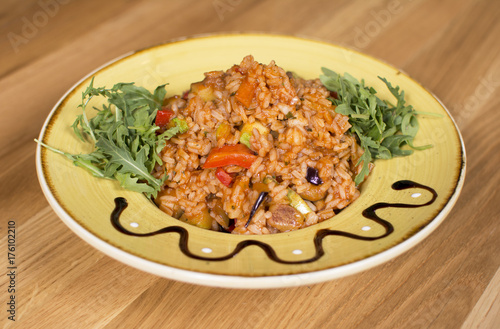 A plate of rice with vegetables. Appetizing healthy rice with vegetables in white plate on a wooden background.