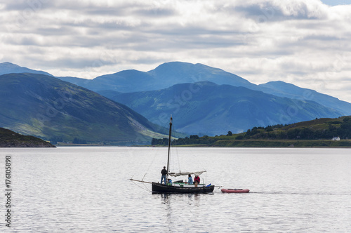 Ullapool, Scotland - August 15, 2010: People in a small sailing boat in front of the small village of Ullapool in the Highlands in Scotland, United Kingdom