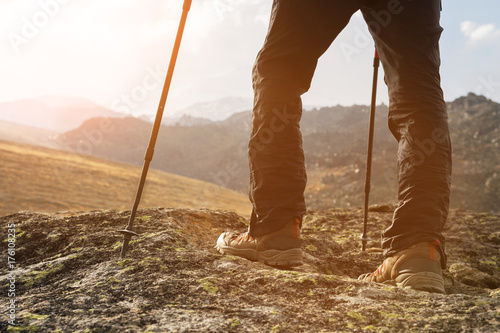Close-up of male legs in trekking boots with sticks for Nordic walking against the background of rocks and distant Caucasian lands