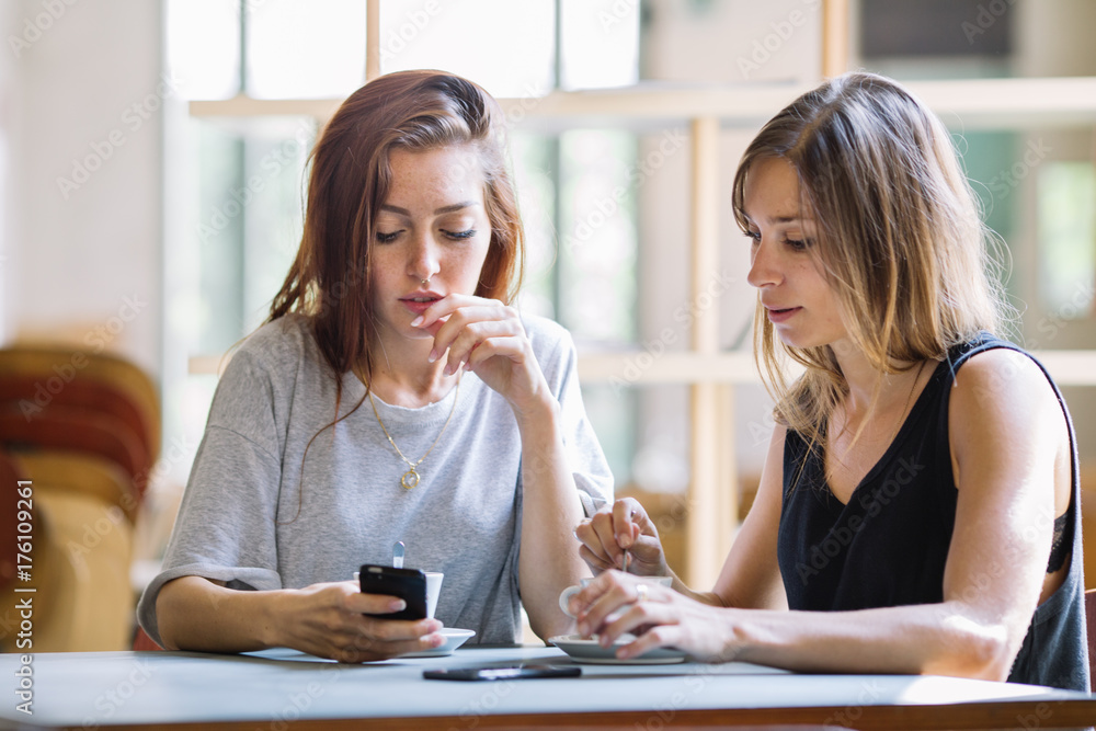 Young caucasian girls watching at the smartphone at the bar Young caucasian girls watching at the smartphone at the bar
