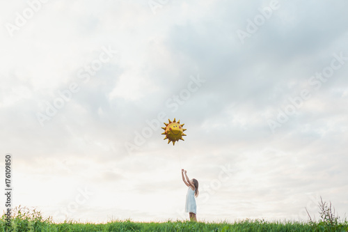 Little girl reaching out to big sun balloon against cloudy sky