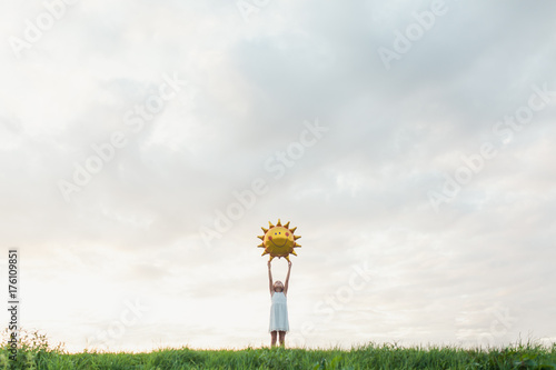 Little girl with a big sun balloon against a cloudy sky photo