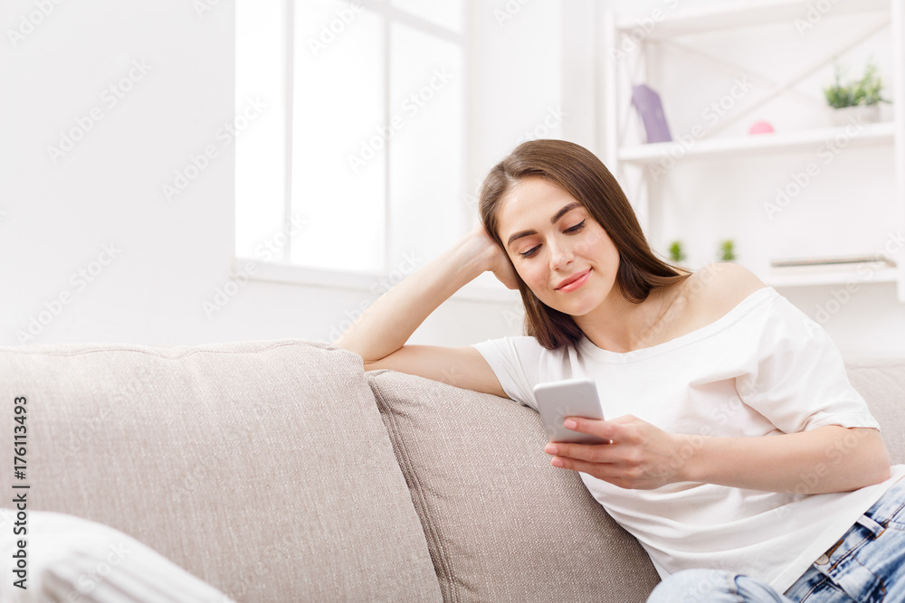 Young woman using smartphone at home on the couch. Dark-haired girl in casual texting online Young woman using smartphone at home on the couch. Dark-haired girl in casual texting online