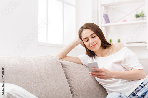 Young woman using smartphone at home on the couch. Dark-haired girl in casual texting online