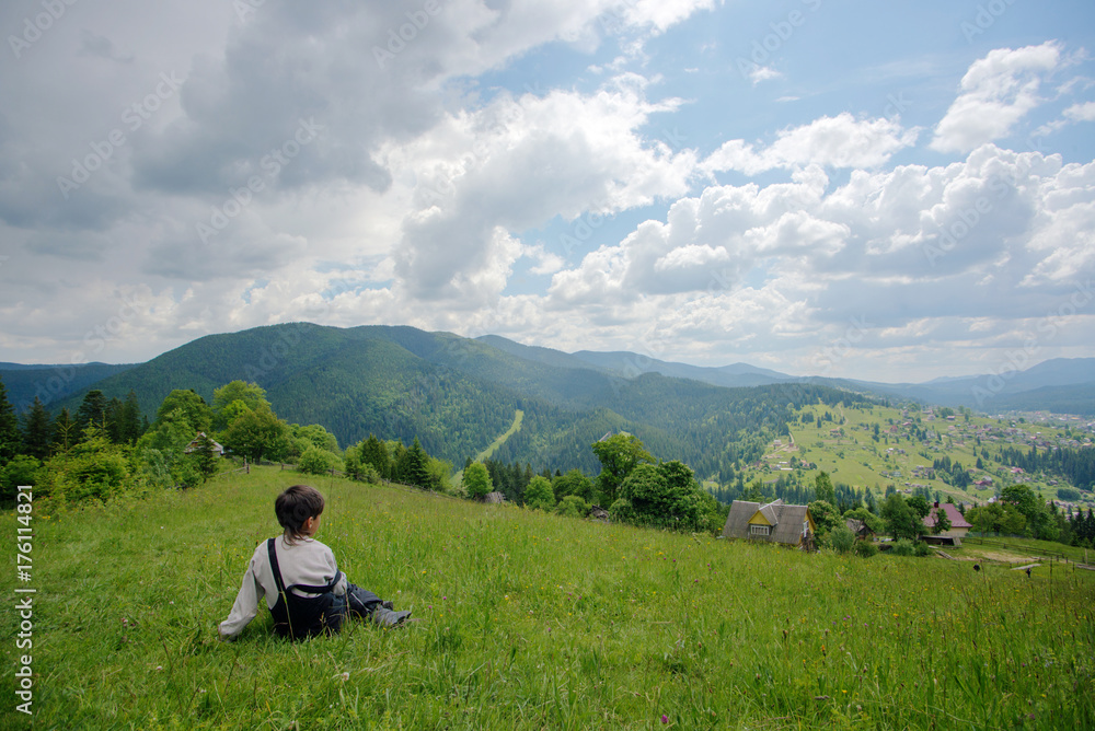 A boy sitting at the top of the hill and looking on mountains