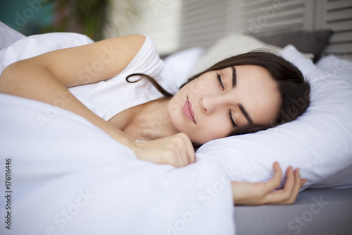 Beautiful young brunette woman sleeping in a white bed.