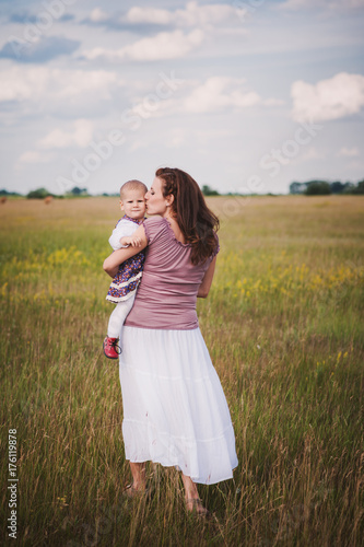 Mother holding her baby daughter in her arms walking on an open field photo