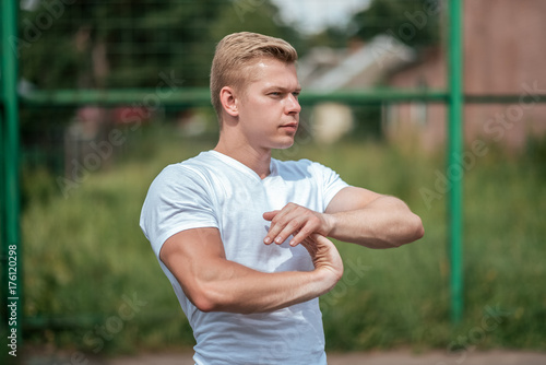 Stretches the muscles of the fingers fingers. A male coach does a warm-up  in a city in nature  in summer T-shirt. Athlete in nature. The concept of a healthy lifestyle. Exercise in the fresh air.