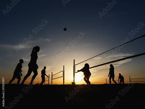 People playing beach volleyball at sunset