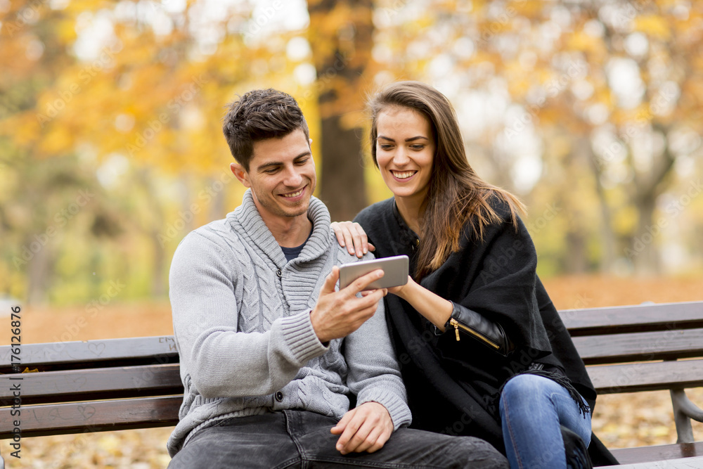 Young couple happily watching something on a smartphone and sitting on bench Young couple happily watching something on a smartphone and sitting on bench