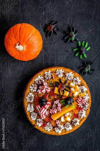 Gummy spiders crawls toward pie for halloween on black background top view
