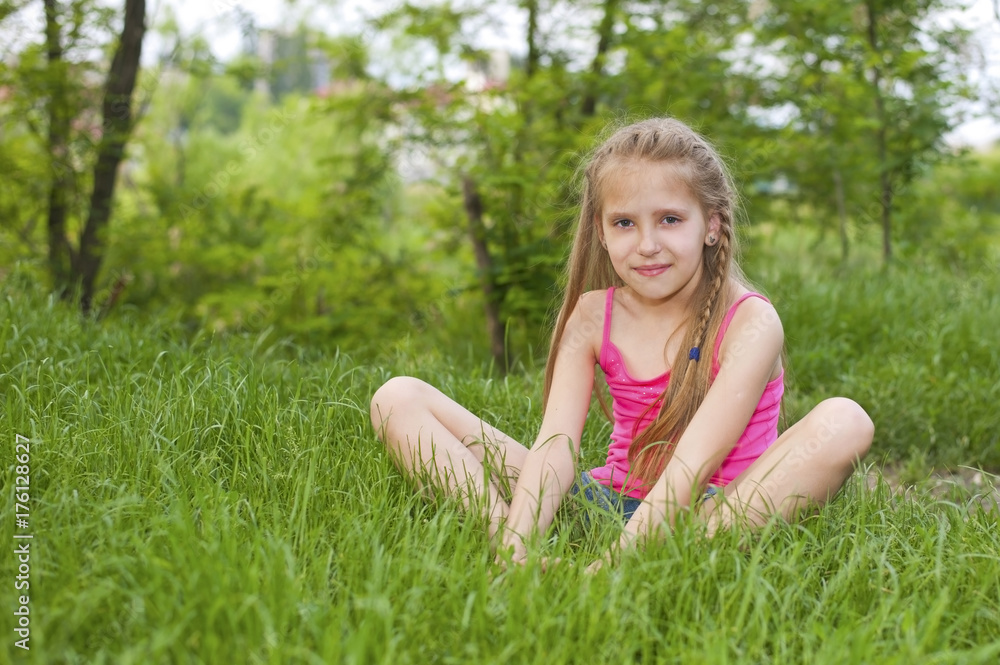 A beautiful young girl sits on a green grass in a yoga pose and smile