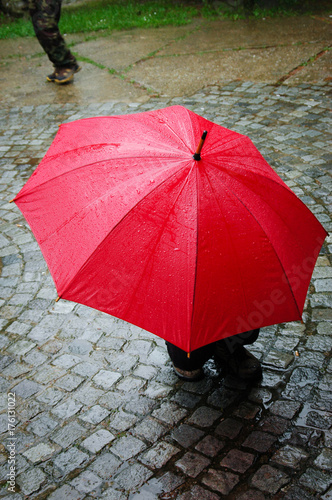 isolated red umbrella in rainy day on cobblestone street 