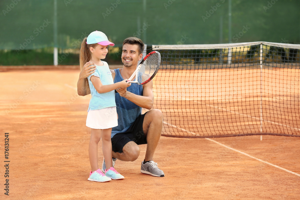 Young trainer with little girl on tennis court