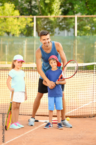 Young trainer with little children on tennis court