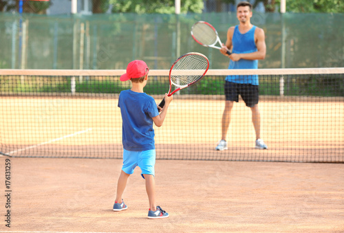 Young trainer with little boy playing tennis on court