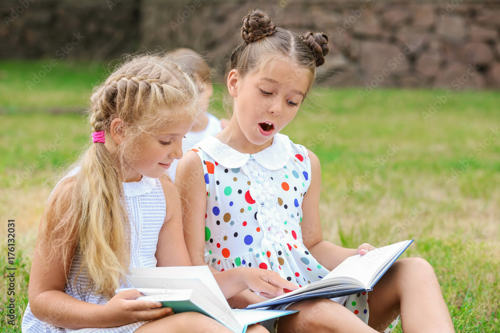 Cute little girls reading books in park Cute little girls reading books in park