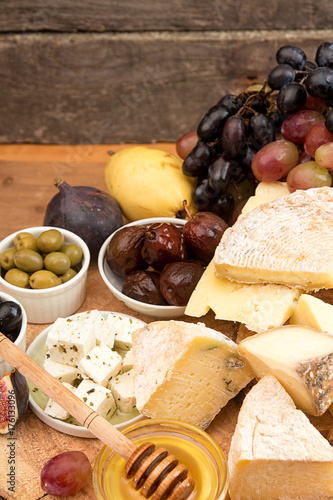 Food composition with blocks of moldy cheese, pickled plums, honey, grape bunch, olives, figs, pear, crackers on wooden background.