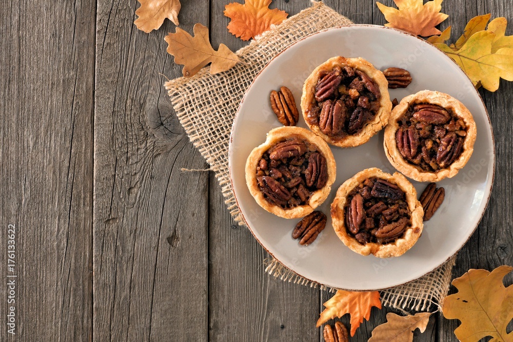 Plate of mini pecan pie tarts, rustic overhead table scene on a wood background Plate of mini pecan pie tarts, rustic overhead table scene on a wood background
