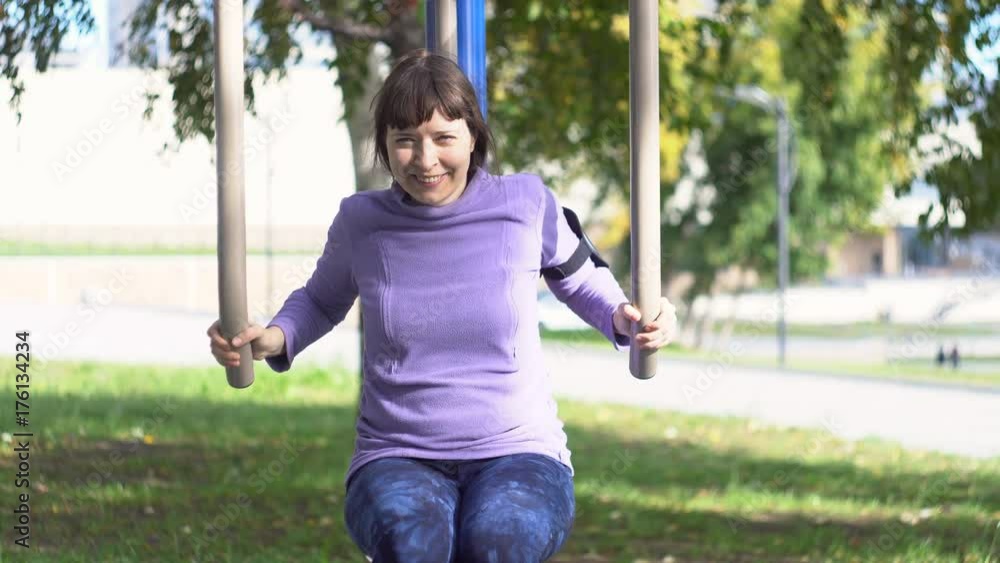 A young woman in sportswear is engaged in fitness on a street simulator in a public park. A person trains simultaneously the muscles of the arms and chest under his own load in the sitting position. A young woman in sportswear is engaged in fitness on a street simulator in a public park. A person trains simultaneously the muscles of the arms and chest under his own load in the sitting position.