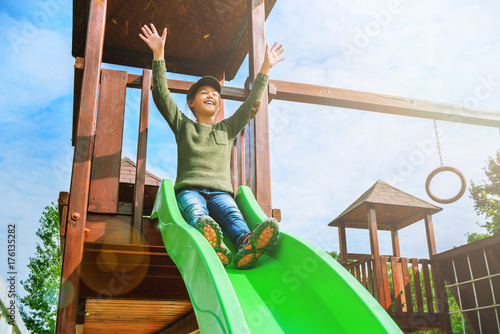 fearless little girl sliding on playground alone in sunny weather photo